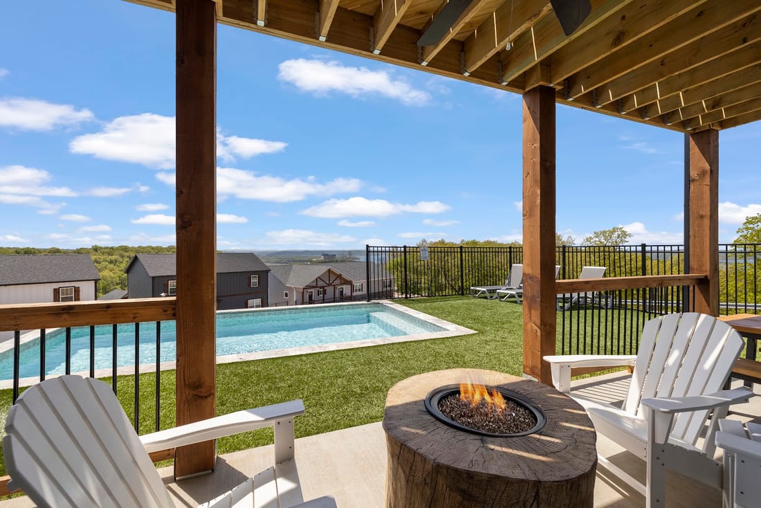 Covered patio with a gas fire pit and lounge chairs beside a fenced pool