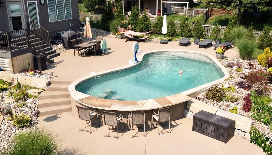 Freeform pool with a tanning ledge framed by patio furniture and plantings