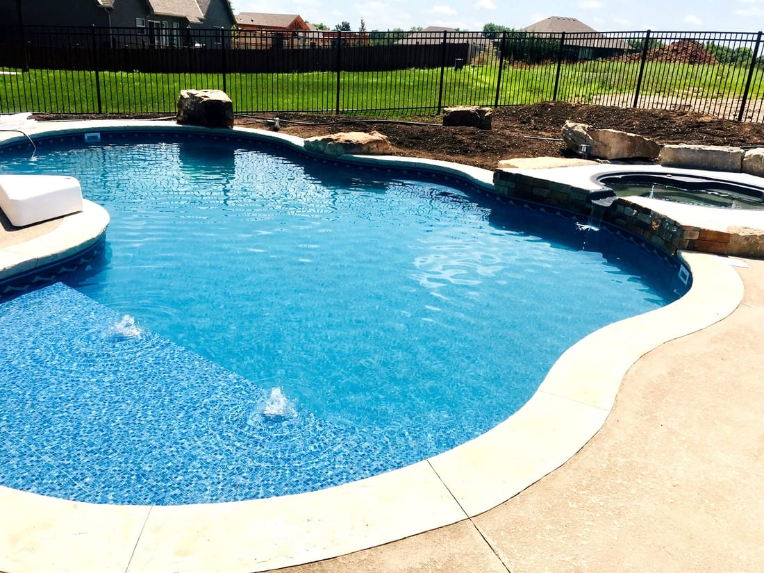 Freeform blue swimming pool with a paver deck and lounge seating