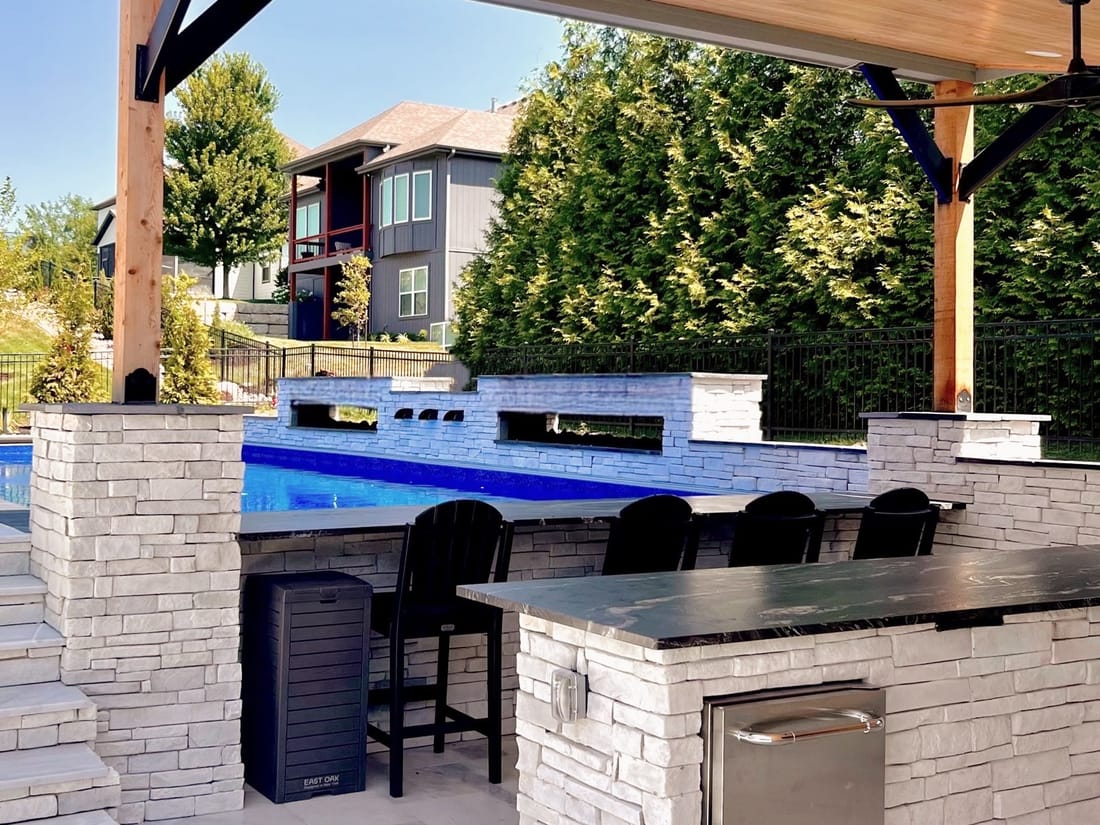 Stone outdoor kitchen and bar with an LED-lit counter and stools